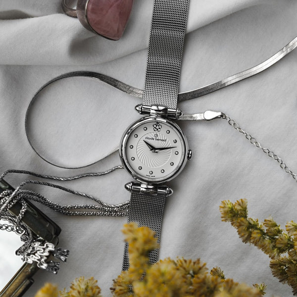 A pendant watch laid out with a silver chain and dried flowers